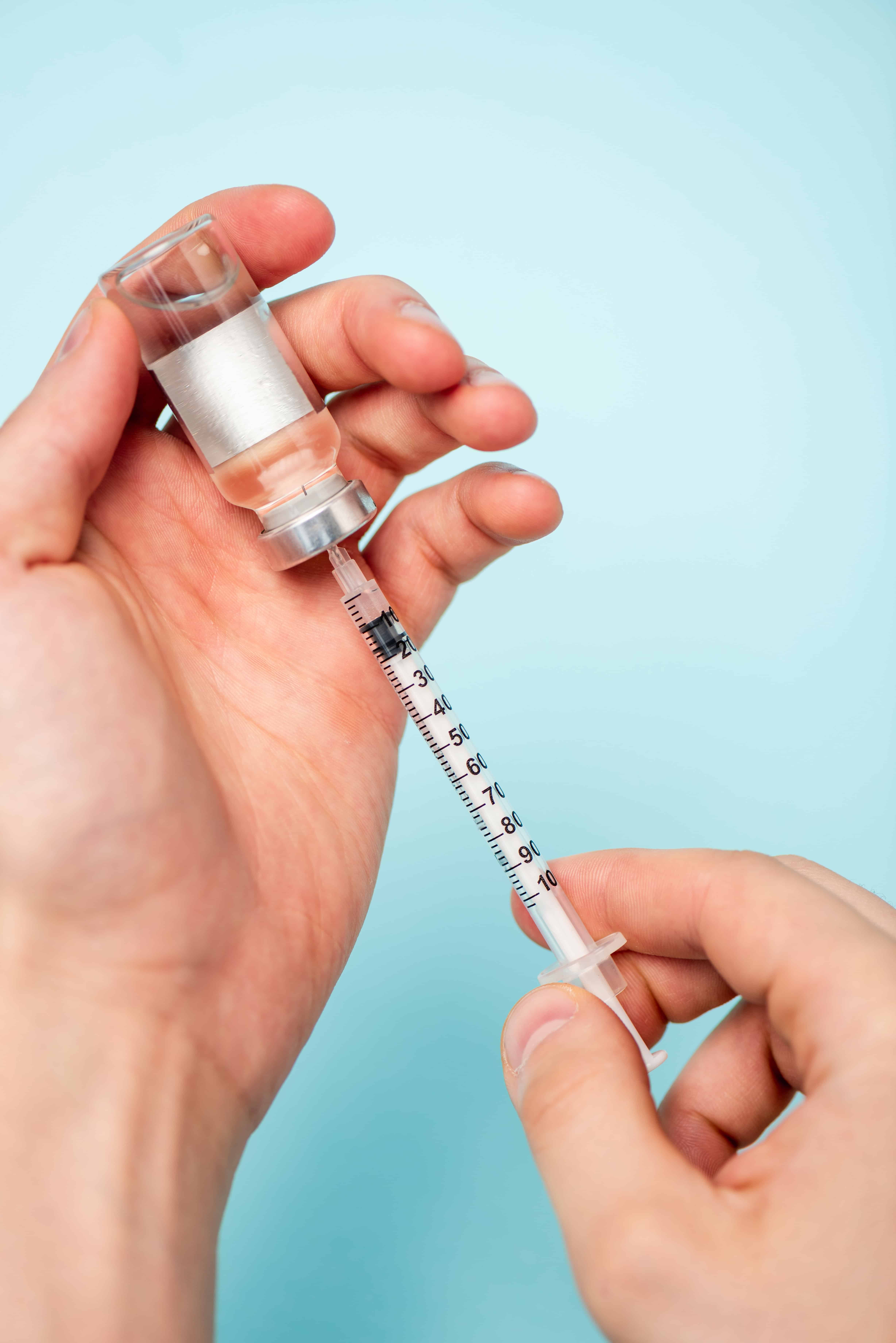 Cropped view of man picking up hormonal drug from jar in syringe on blue surface