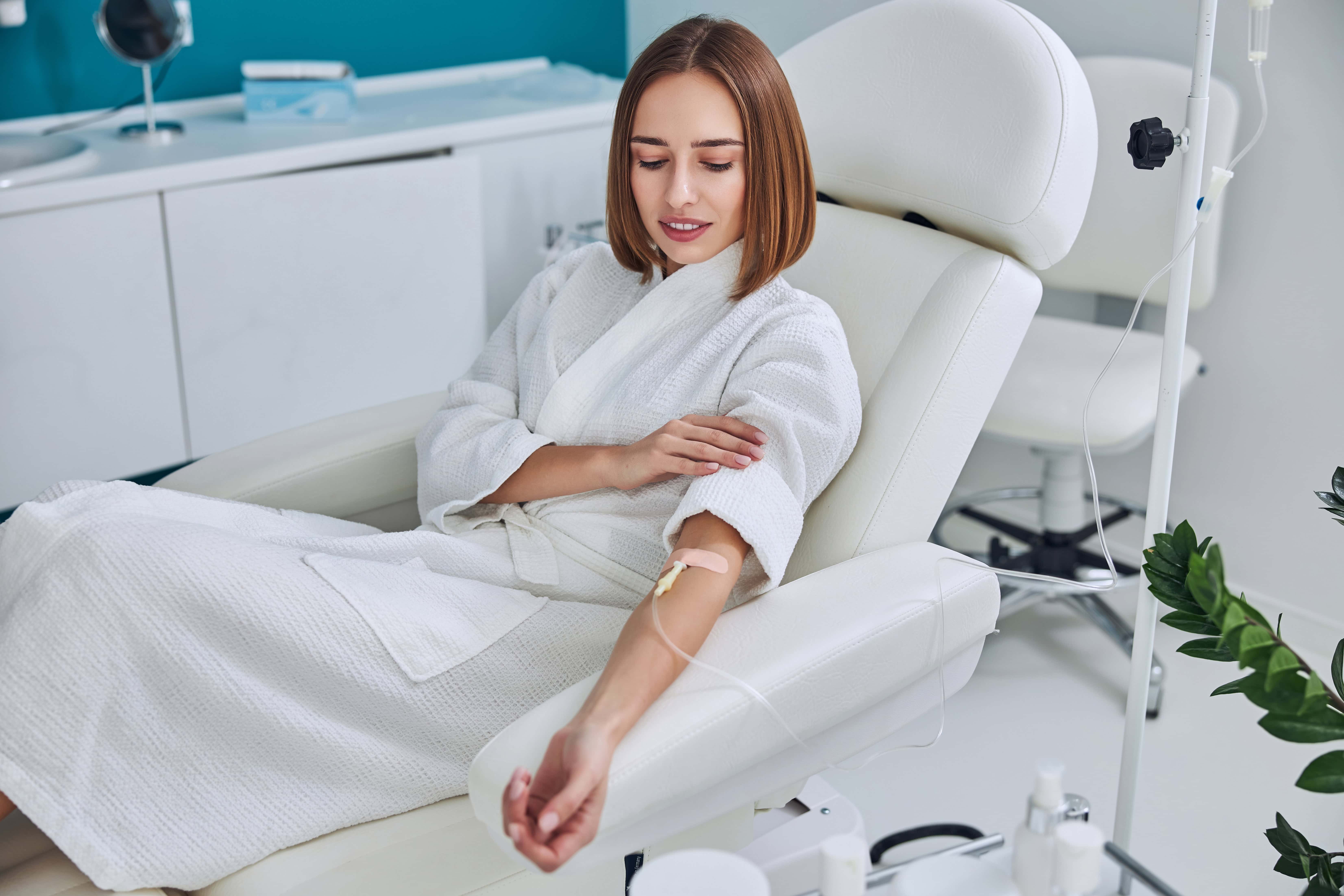 Happy cheerful young lady resting at the intravenous vitamin drip treatment in spa salon