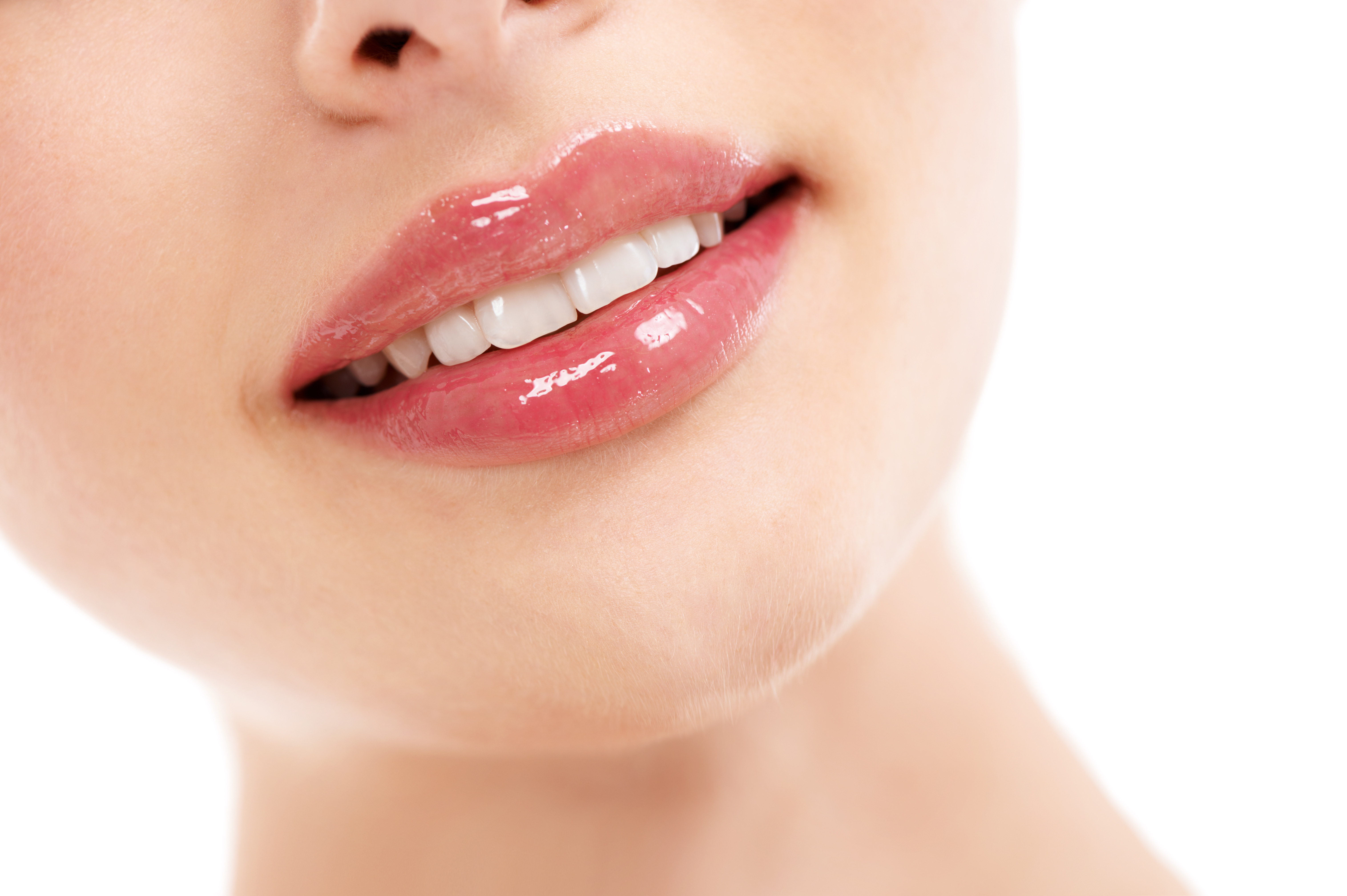 Lips of gloss. Cropped image of a womans smiling mouth against a white background.