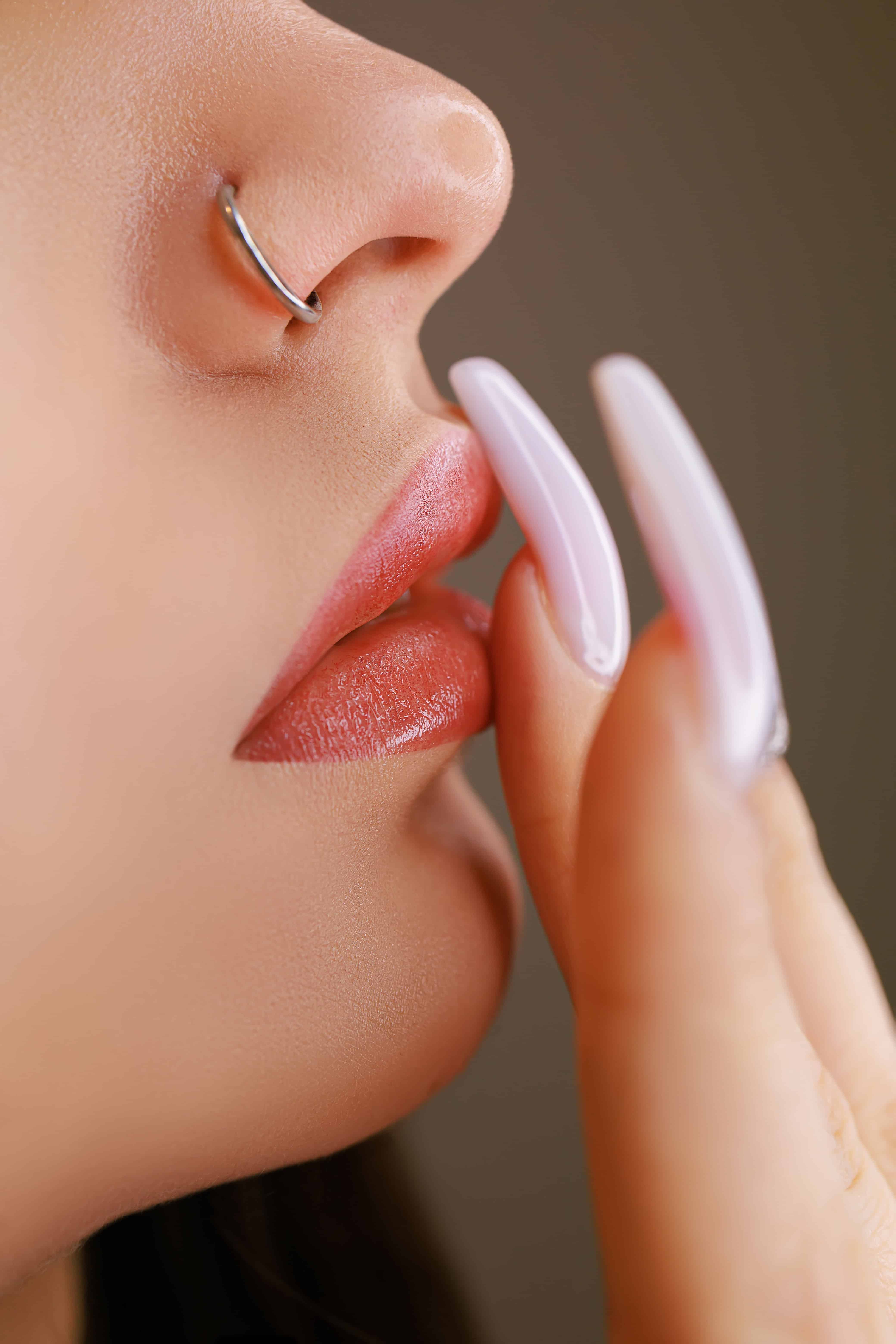 Macro photo of girl's lips after permanent lip makeup. Girl touches lips with fingers after tattoo.