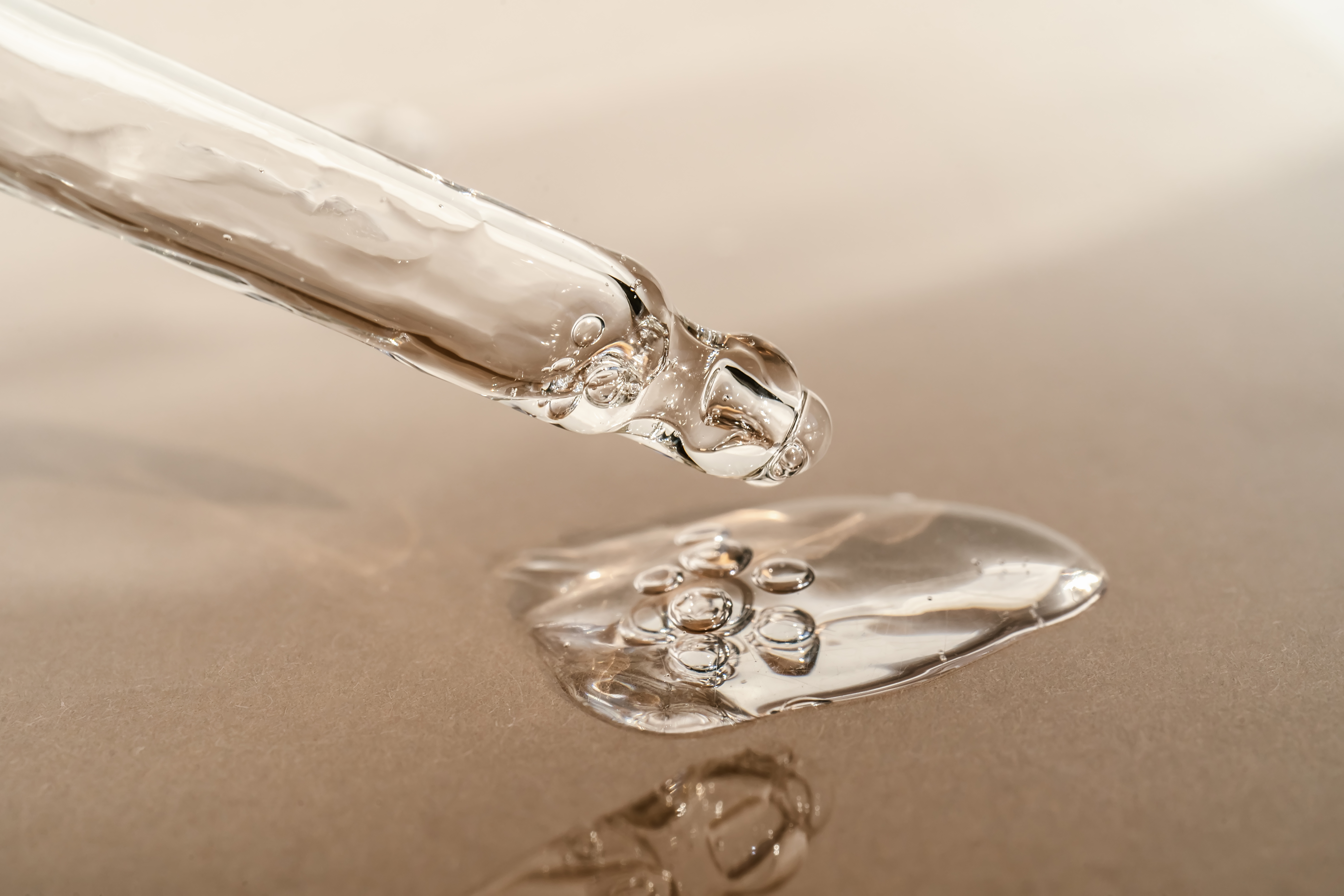 The texture of serum or oil with a pipette on a beige background.