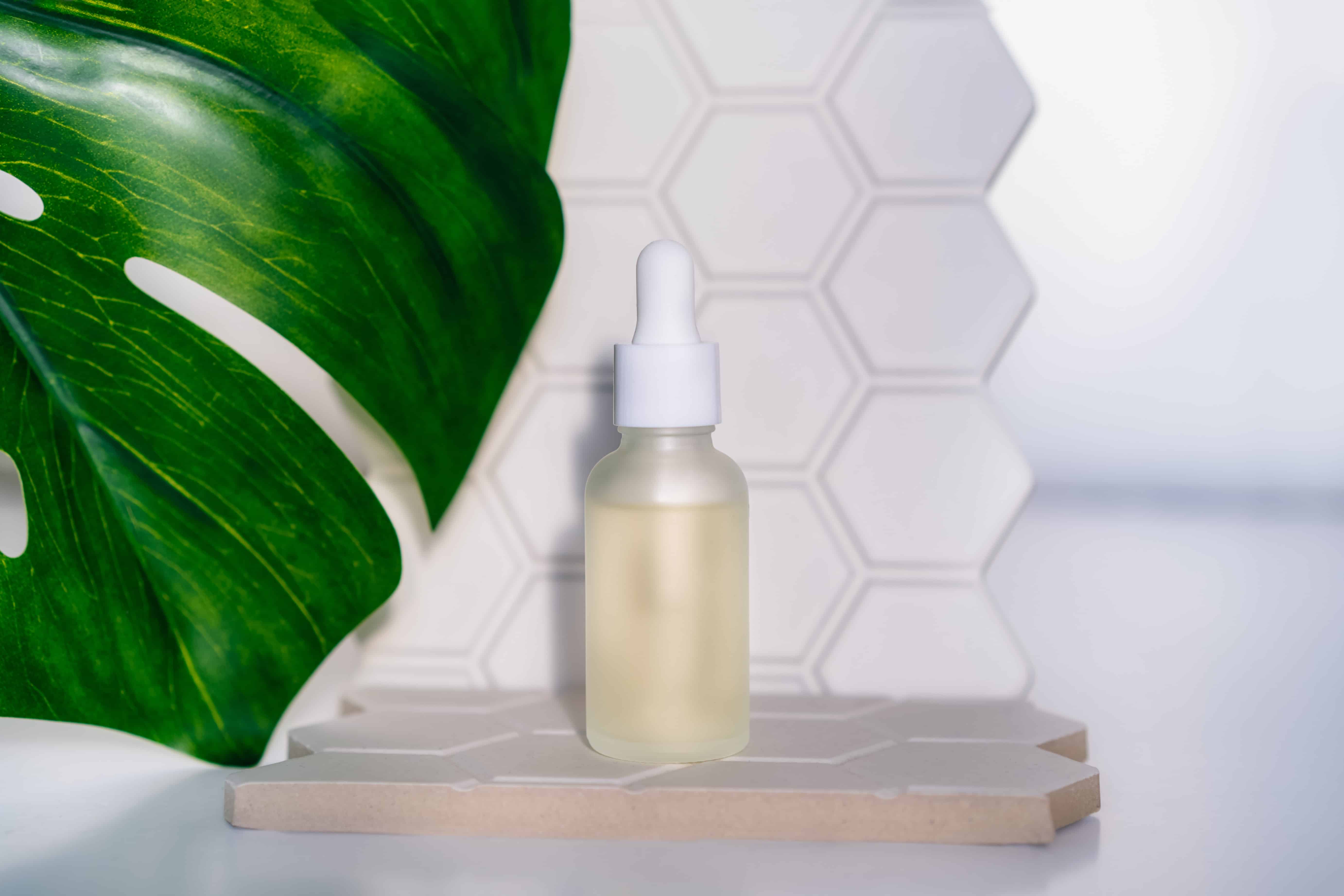 Mockup bottle of natural essential oil on geometric hexagon cell shapes background with a monstera