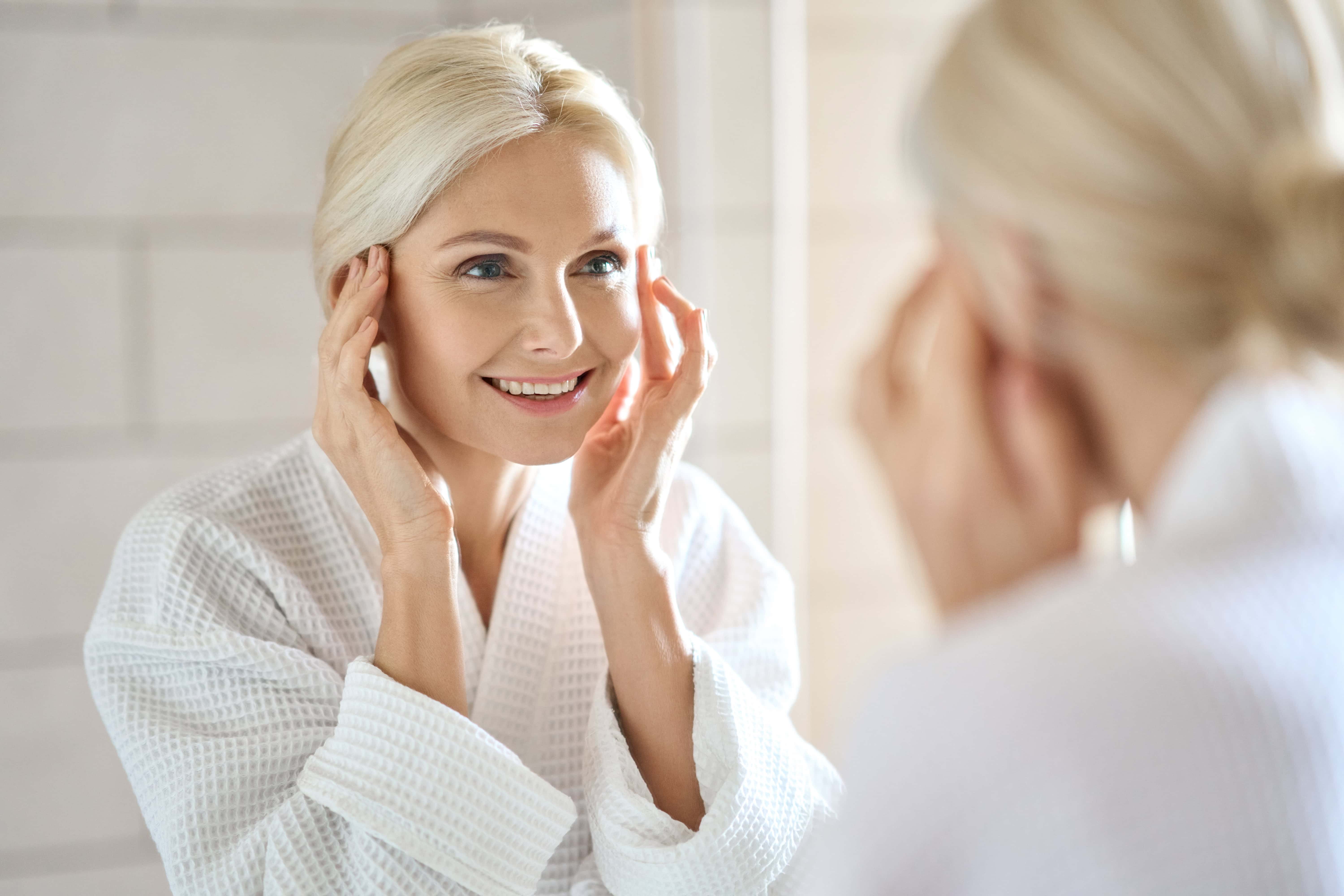 Attractive mid age woman smiling looking at mirror. Skincare concept.